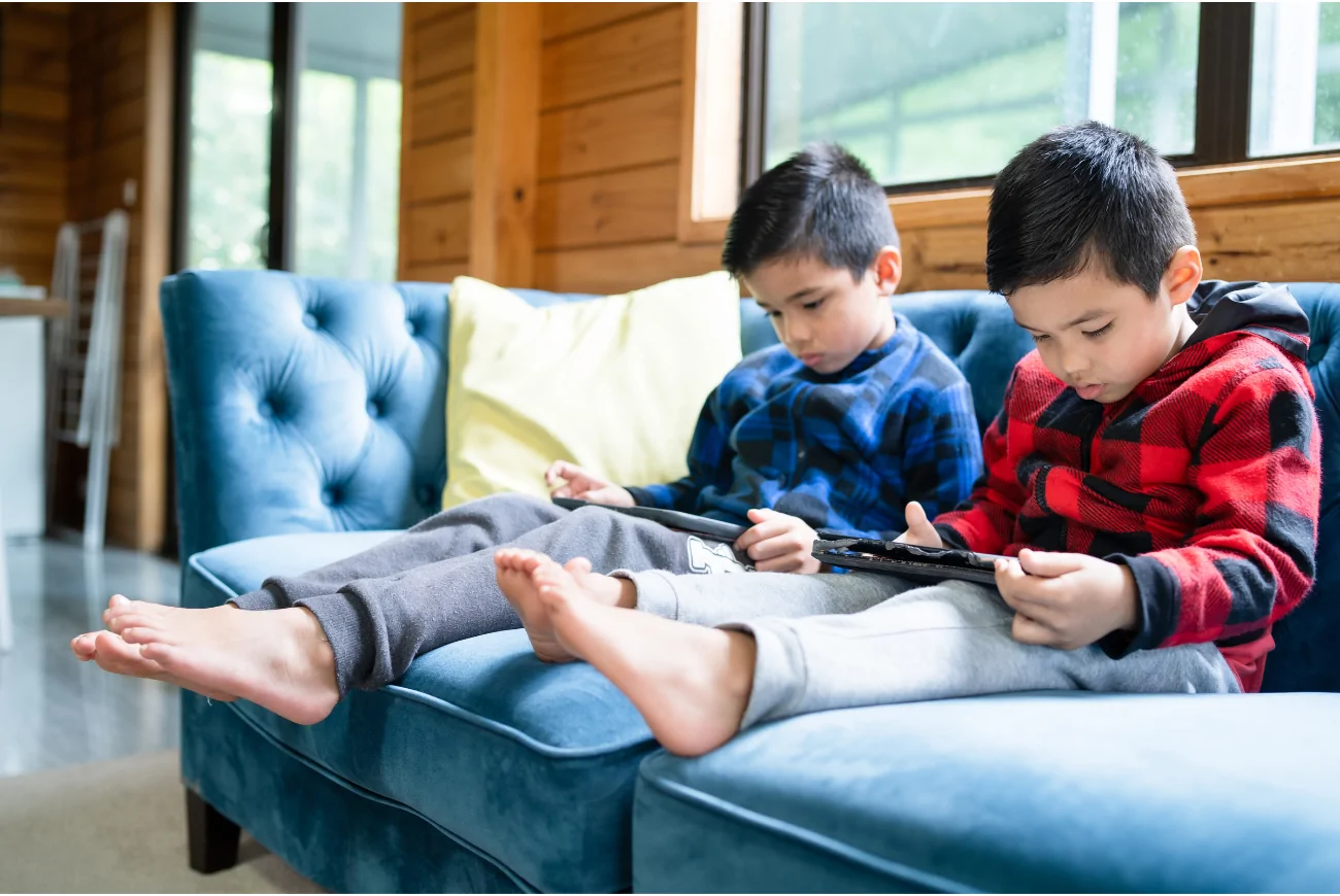 two children sit on a sofa watching something on their phones