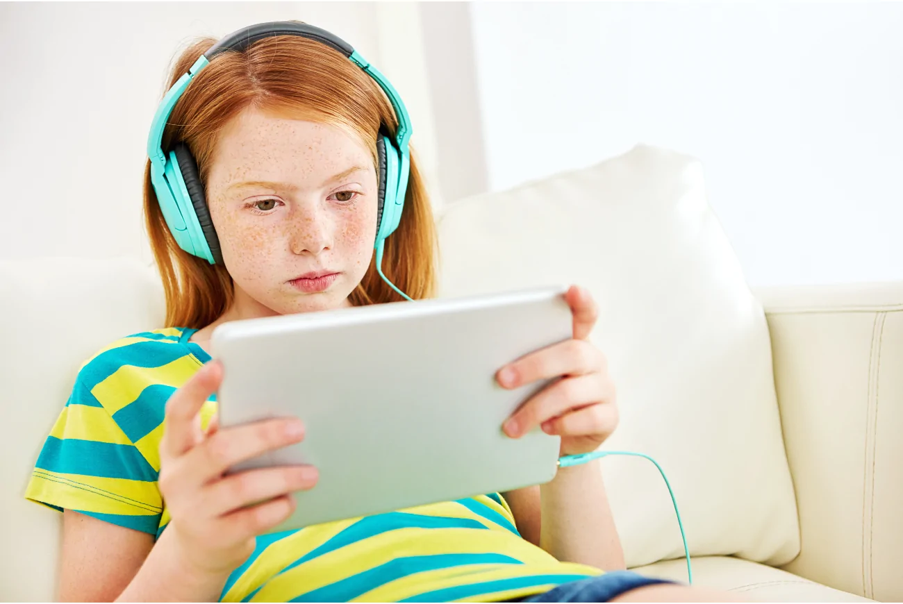 Child sat on ipad with headphones on.