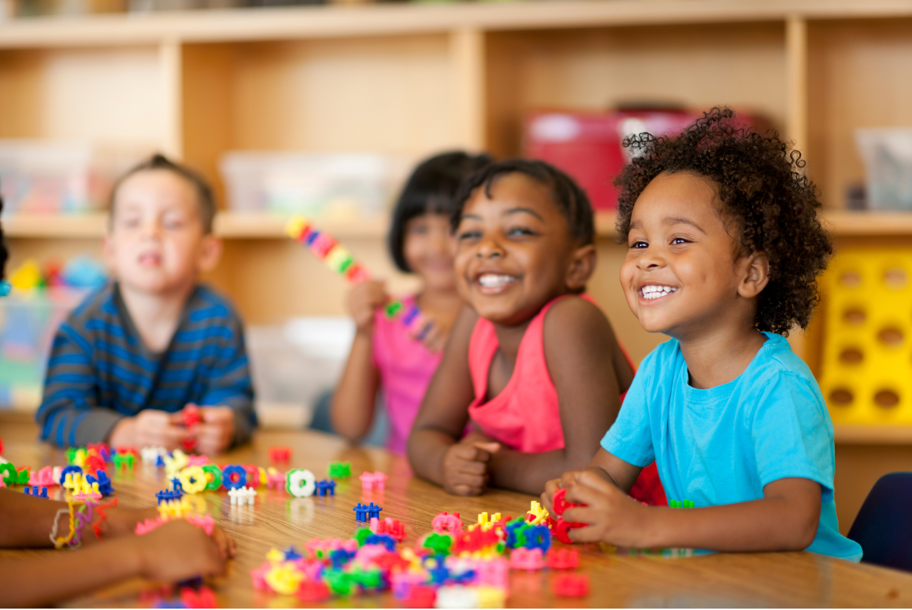 Diverse children sit at a table together with toys.