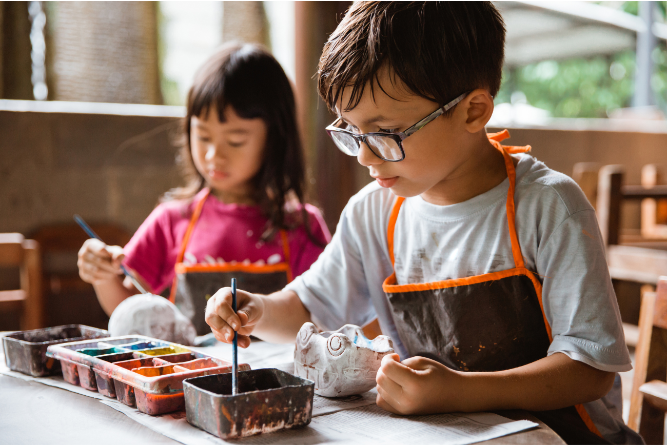 Two kids sit together doing arts and crafts.