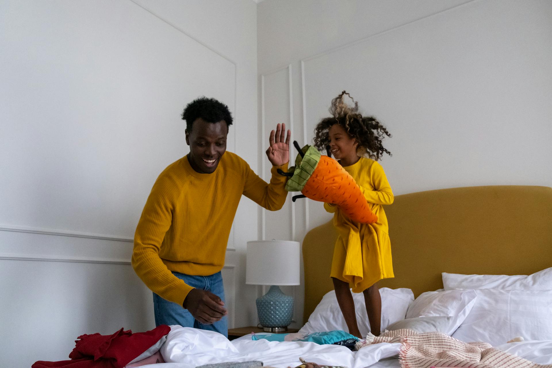 A girl stands on the bed playing with her father.