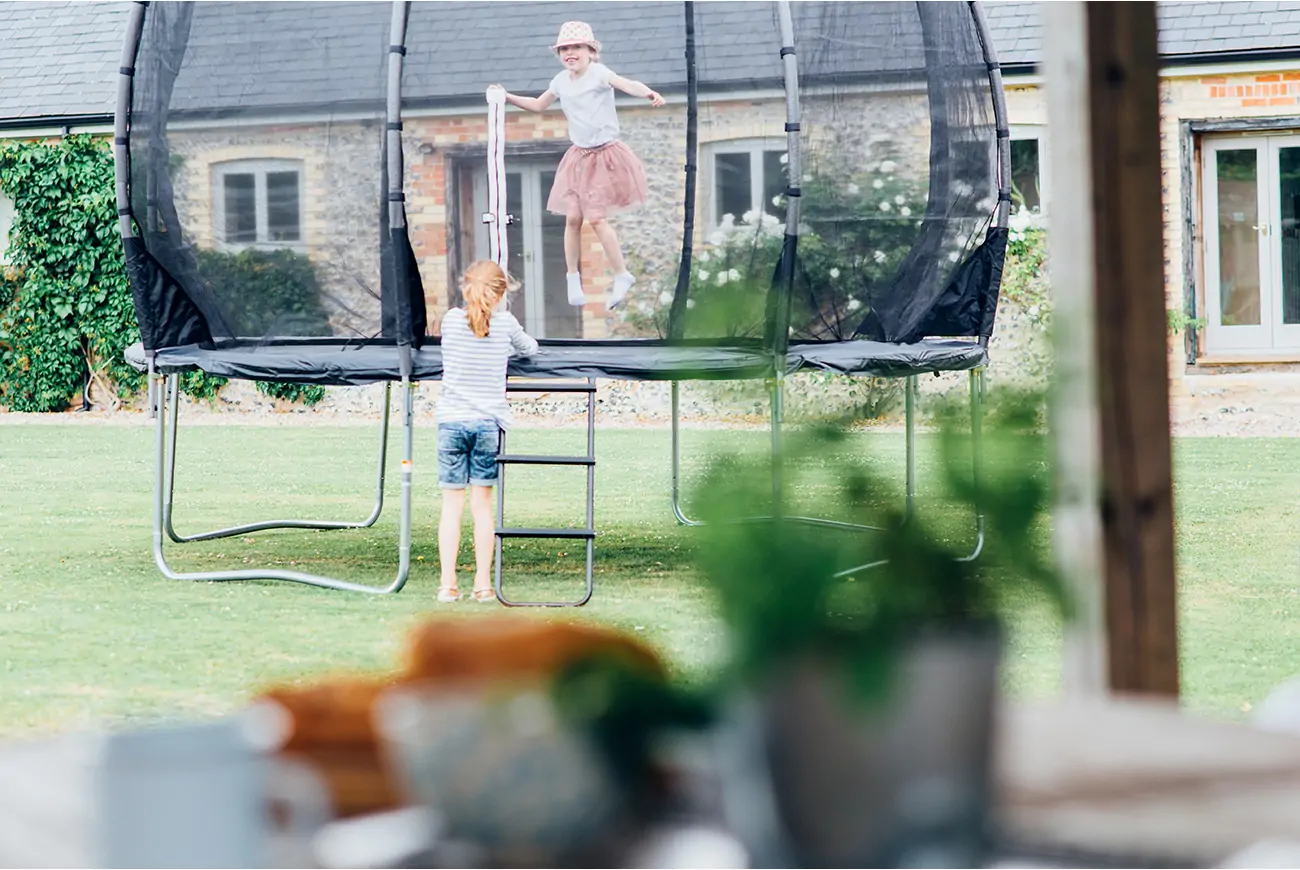 Children jump on trampoline in a garden.