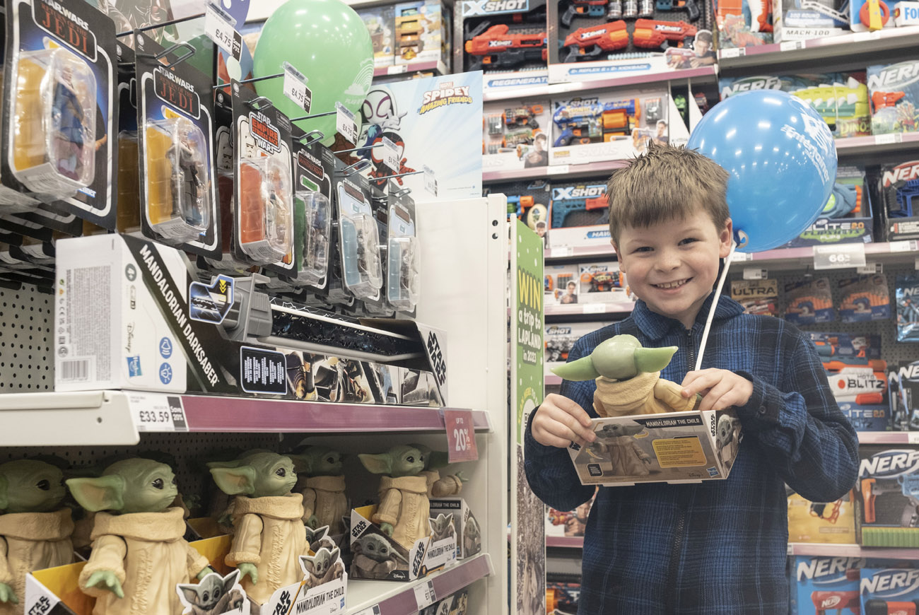 Child holding baby Yoda toy in The Entertainer store.