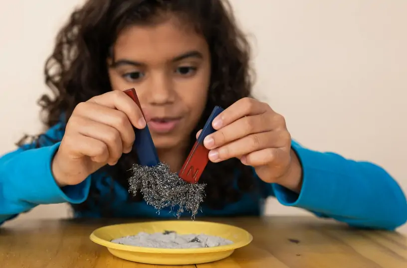 Child playing with two magnets over a plate, one is positive and one is negative so they each push against each other.