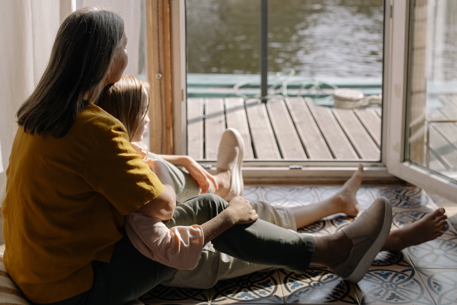 Mother and daughter sit on floor and watch out the window.